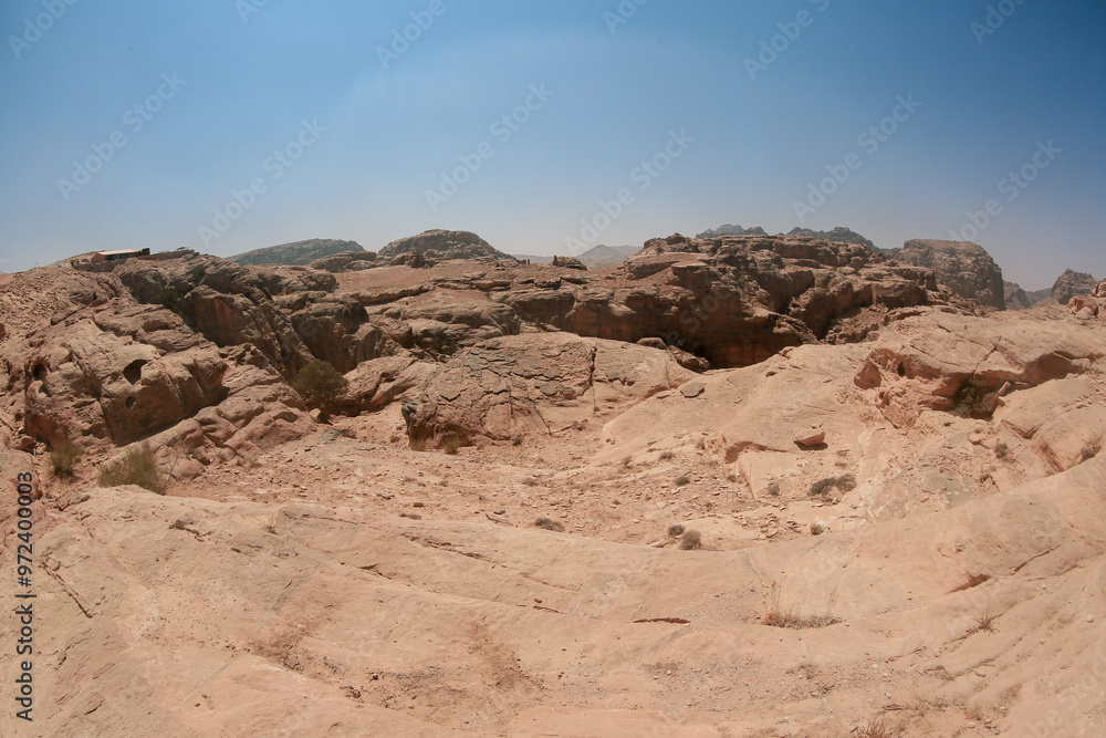 Exploring the ancient and rugged landscape of Petra, Jordan under a clear blue sky during midday sunlight Exploring the ancient and rugged landscape of Petra, Jordan under a clear blue sky during midday sunlight