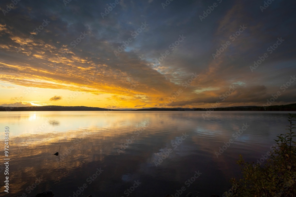Obraz premium Sunset over a calm lake with dramatic clouds and reflections.