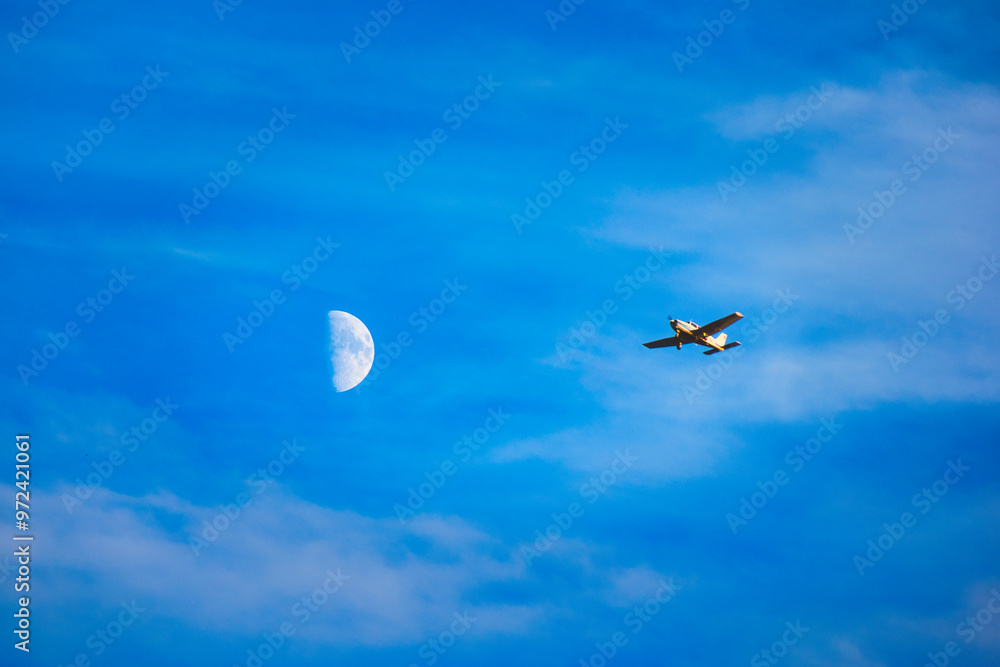 Fototapeta premium Small plane flying near a crescent moon on a blue sky with clouds.