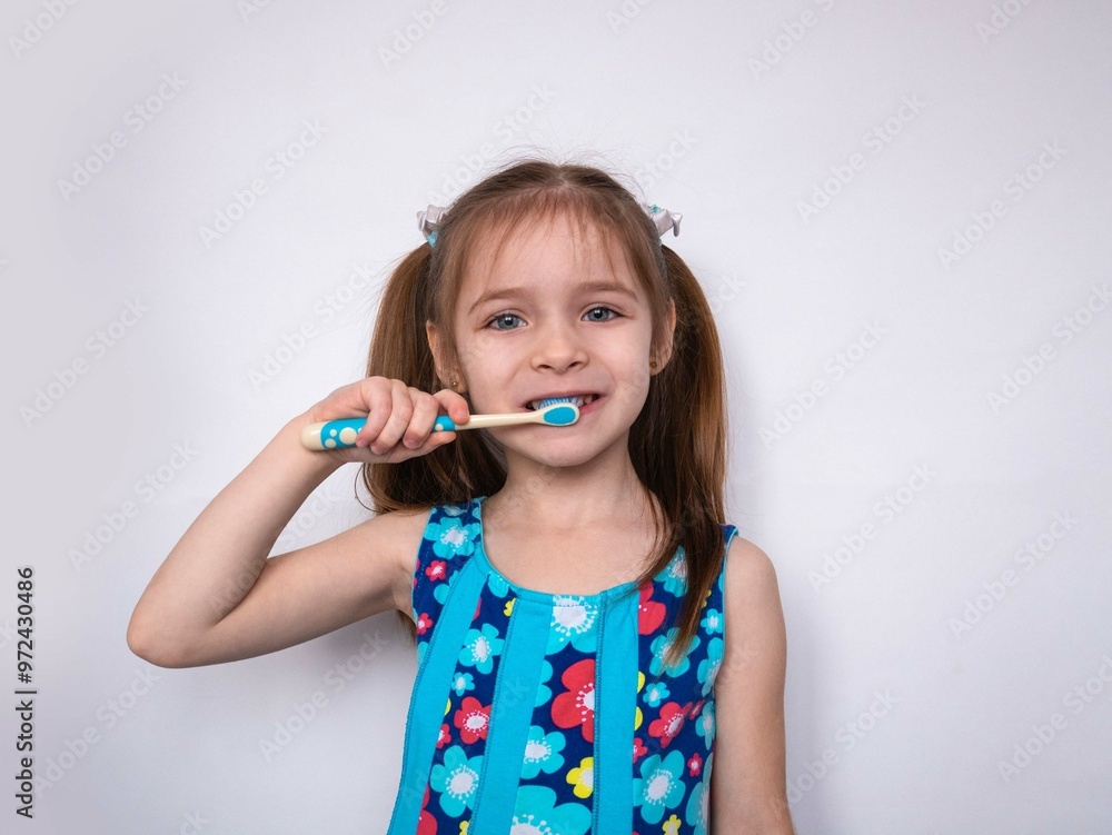 A little blonde girl with ponytails is brushing her teeth, holding a brush in her hand, smiling. The concept of proper oral care, pediatric dentistry A little blonde girl with ponytails is brushing her teeth, holding a brush in her hand, smiling. The concept of proper oral care, pediatric dentistry