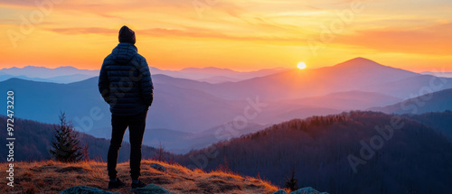 A lone figure stands on a mountain peak, admiring a breathtaking sunset over layered hills and vibrant skies.