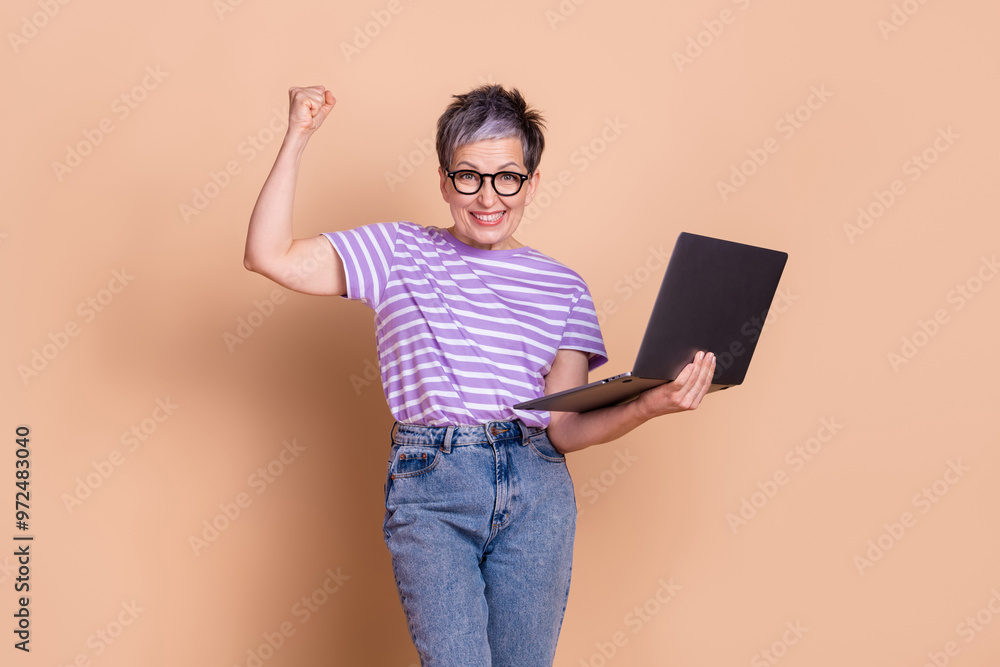 Photo of glad adorable senior woman wear striped stylish clothes raise hand fist isolated on beige color background Photo of glad adorable senior woman wear striped stylish clothes raise hand fist isolated on beige color background