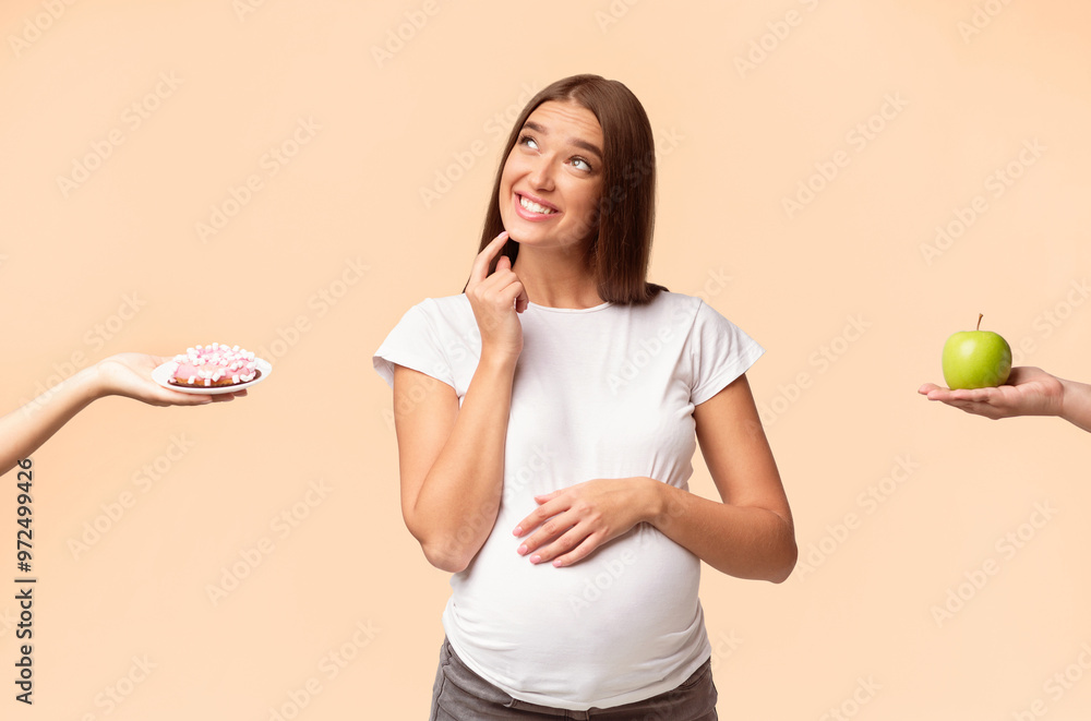 Pregnancy And Diet. Pregnant Lady Dreaming About Sweets Choosing Doughnut Or Apple Posing Over White Studio Background Pregnancy And Diet. Pregnant Lady Dreaming About Sweets Choosing Doughnut Or Apple Posing Over White Studio Background