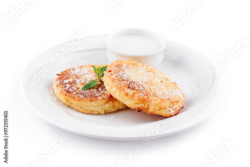 Two golden brown cheese pancakes lying on white plate with sour cream and mint