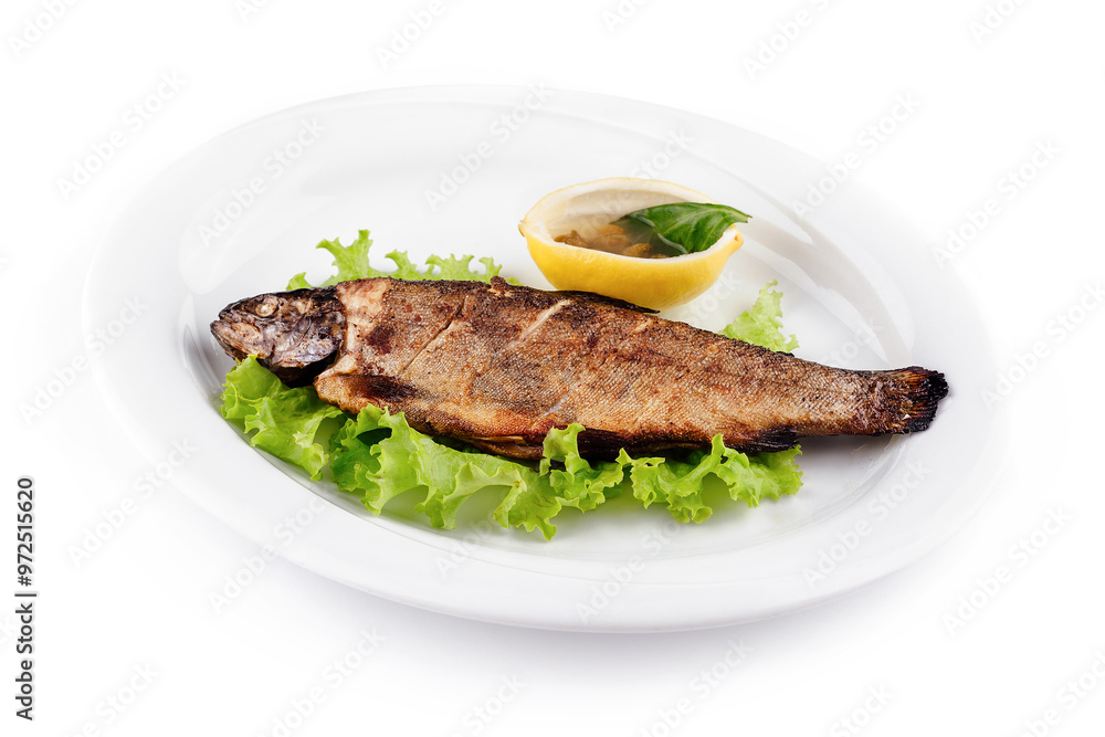 Grilled trout served on bed of lettuce with lemon and condiment Grilled trout served on bed of lettuce with lemon and condiment