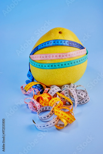 a large pomelo is wrapped in multi-colored measuring tapes on a blue background close-up, vertically, the concept of losing weight, slimness photo