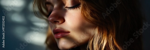 A close-up portrait of a young woman with soft lighting and shadows on her face.