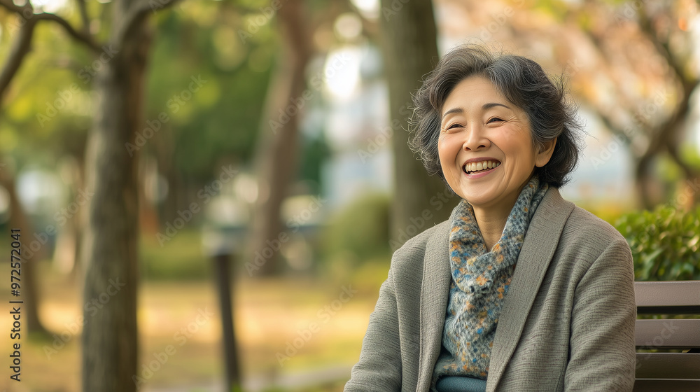 A mature Japanese woman laughing naturally while sitting on a bench in a park , copy space, natural A mature Japanese woman laughing naturally while sitting on a bench in a park , copy space, natural