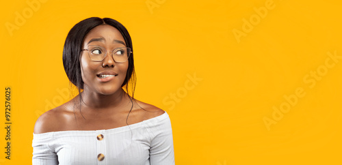 Oops. Millennial Afro Girl Biting Lips Looking Aside Standing Over Orange Studio Background. Panorama, Empty Space For Text photo