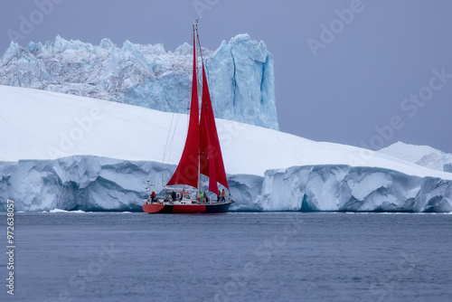 Red sailing boat in front of a giant blue iceberg in Ilulissat Icefjord, Greenland photo