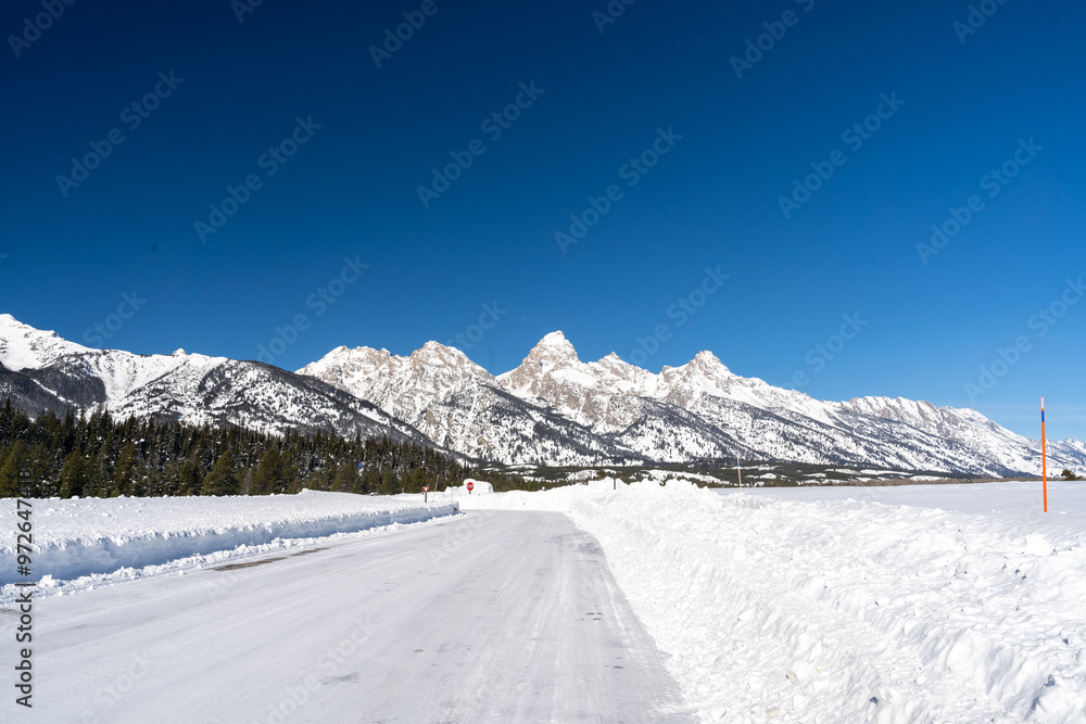 Obraz premium A sunny view of the Teton Mountain Range covered in snow during a cold winter.