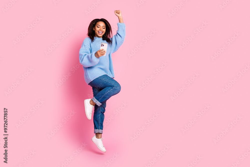 Full body portrait of nice young girl raise fist jump hold phone isolated on pink color background Full body portrait of nice young girl raise fist jump hold phone isolated on pink color background