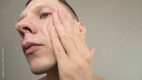 Young man applying aftershave gel on a light background in a close-up shot