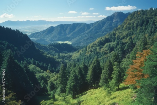 a breathtaking view of a mountainous landscape. The sky is blue with some clouds, and the mountains are covered with lush green trees.