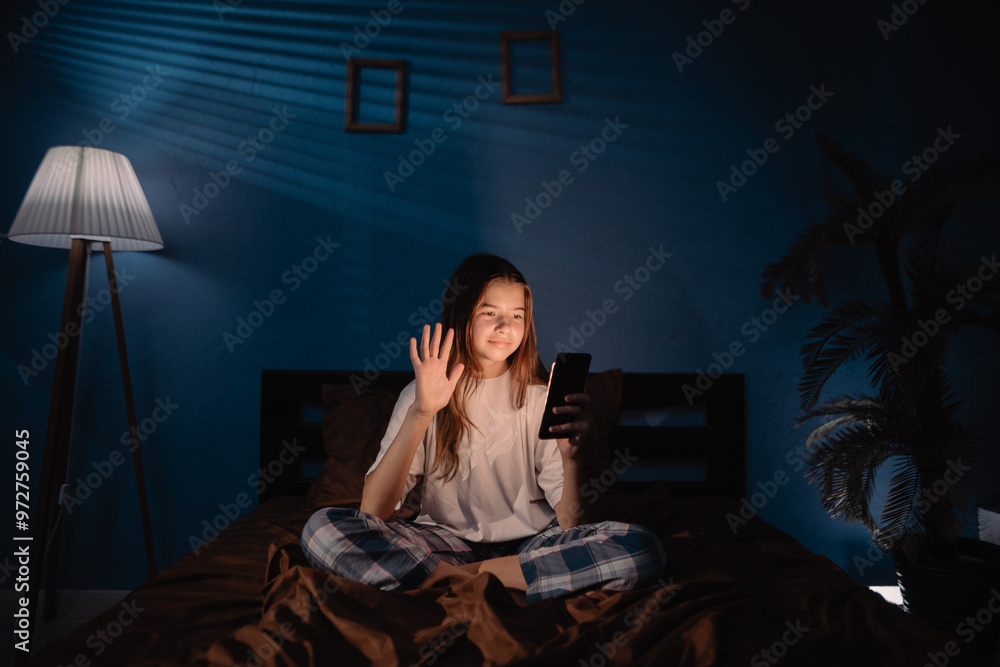 young girl sitting in bed at night, having video call using smart phone young girl sitting in bed at night, having video call using smart phone