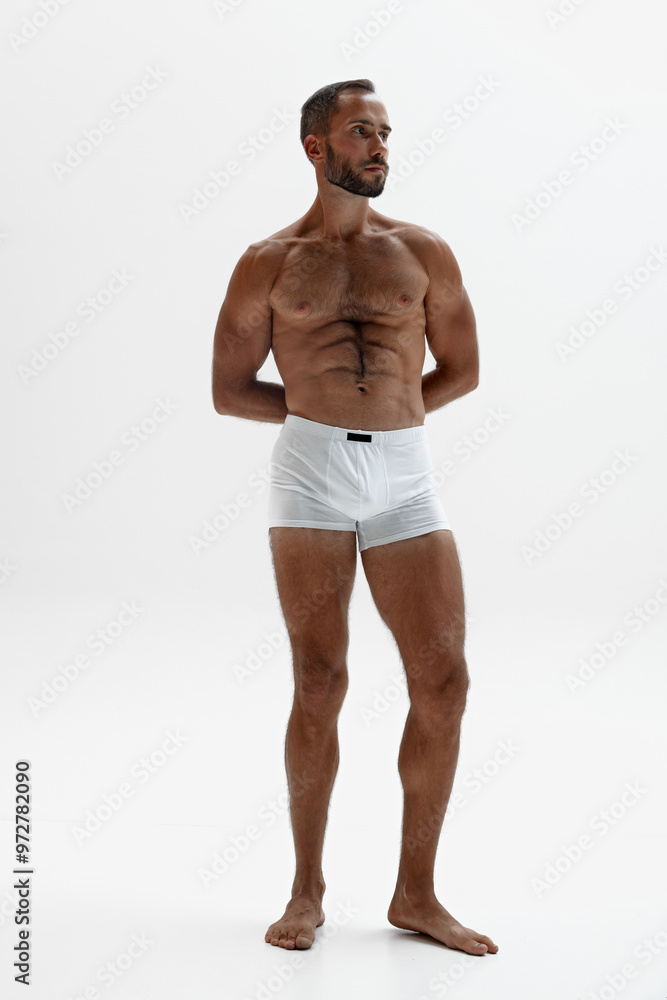 Man stands with his hands clasped behind his back, his poised, confident stance exudes control and calm against white background. Concept of beauty and fashion, style and youth, male health. Man stands with his hands clasped behind his back, his poised, confident stance exudes control and calm against white background. Concept of beauty and fashion, style and youth, male health.