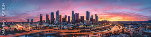 Modern cityscape of Los Angeles City with skyscrapers and highways, Los Angeles river in the background at dusk, illuminated by street lights. A Vincent Thomas bridge connecting two parts of downtown