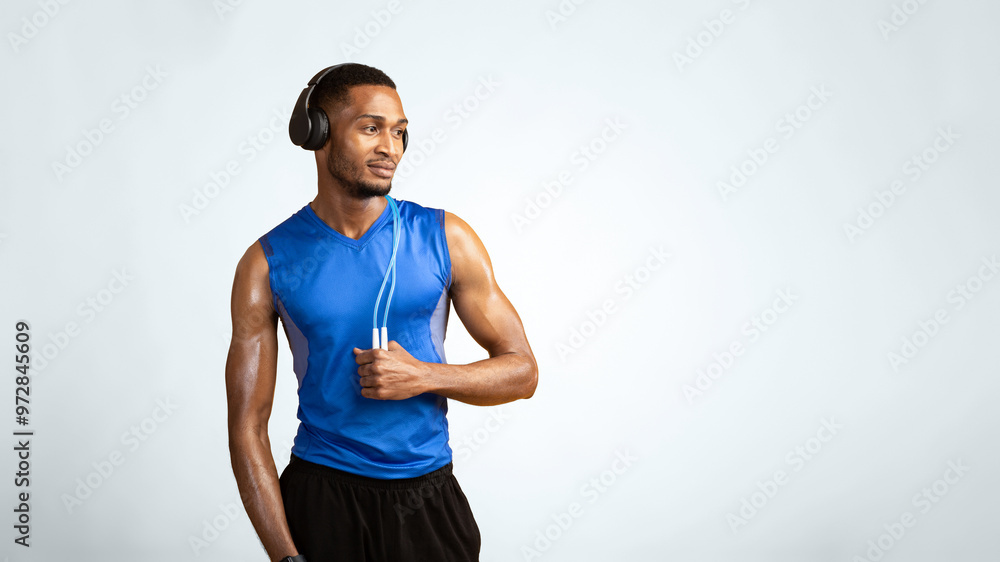 Fitness Model. Confident afro man wearing headphones and holding jumping rope on neck over yellow studio wall, copyspace Fitness Model. Confident afro man wearing headphones and holding jumping rope on neck over yellow studio wall, copyspace