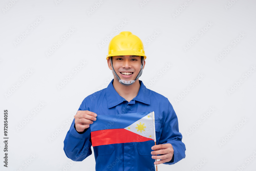 A Filipino seaman or construction worker in blue coveralls and a yellow hard hat proudly holds the Philippine flag, symbolizing national pride and dedication. Isolated on a white background. A Filipino seaman or construction worker in blue coveralls and a yellow hard hat proudly holds the Philippine flag, symbolizing national pride and dedication. Isolated on a white background.