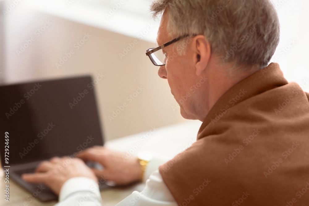 Fototapeta premium Unrecognizable Senior Gentleman Working On Laptop Sitting At Workplace. Selective Focus, Back View