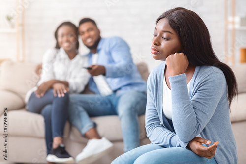 Sad african girl envy to her dating friends that watching tv together on sofa on background, selective focus