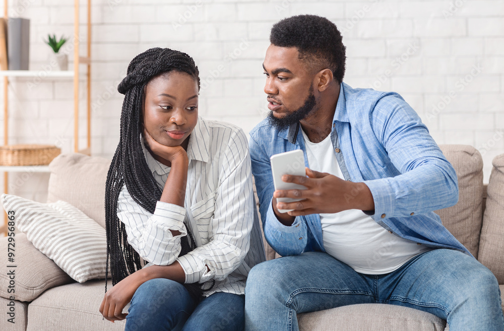 Cheating And Infidelity Concept. Jealous Boyfriend Showing His Unfaithful Girlfriend Her Phone With Message From Stranger, Sitting On Sofa At Home Cheating And Infidelity Concept. Jealous Boyfriend Showing His Unfaithful Girlfriend Her Phone With Message From Stranger, Sitting On Sofa At Home