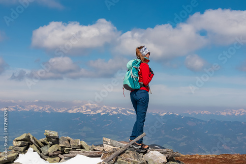 Hiker woman standing on rock formation atop of mountain peak Lenzmoarkogel, Gleinalpe, Lavanttal Alps, Styria, Austria. Hiking trail on snow covered alpine meadow. Wanderlust. Tranquil serene scene photo