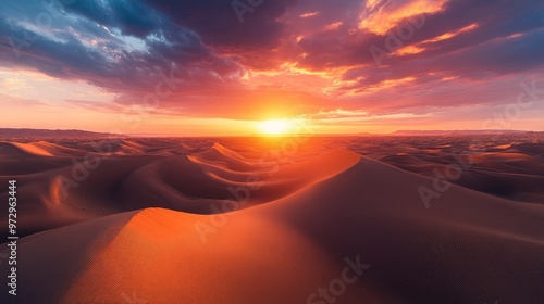 A panoramic view of a sunrise over an expansive desert, with the sun casting long shadows across the dunes and the sky painted in vibrant hues of orange and pink.