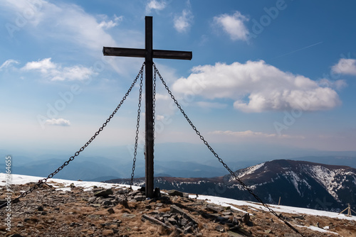 Wooden summit cross standing atop remote mountain peak Lenzmoarkogel, Gleinalpe, Lavanttal Alps, Styria, Austria. Hiking trail over snow covered alpine meadow. Wanderlust. Tranquil serene atmosphere photo