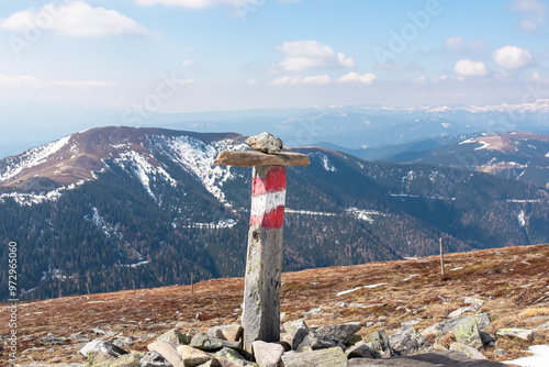 Red white flag painted on trail marker along scenic hiking trail over snow covered alpine meadow on Gleinalpe, Lavanttal Alps, Styria, Austria. Panoramic view of majestic snow-capped mountains in fall photo