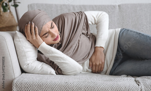 Sick Muslim Woman In Hijab Having Acute Abdominal Or Menstrual Pain, Lying On Couch At Home