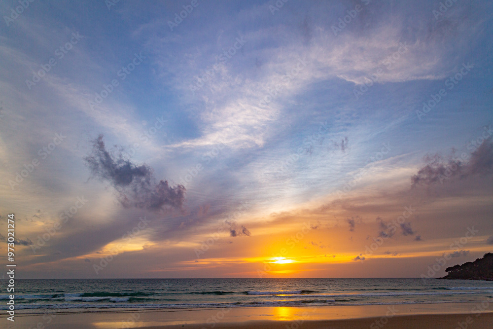Fototapeta premium A stunning sunset over the ocean with soft golden light reflecting on the water, featuring silhouettes of people walking along the shore. Water flows from a small stream into the sea.