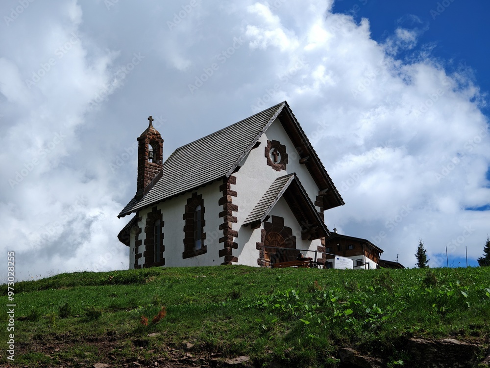 Obraz premium White Chapel on a Green Hilltop, Passo Rolle - A stunning view of a charming chapel nestled amidst the breathtaking Dolomites