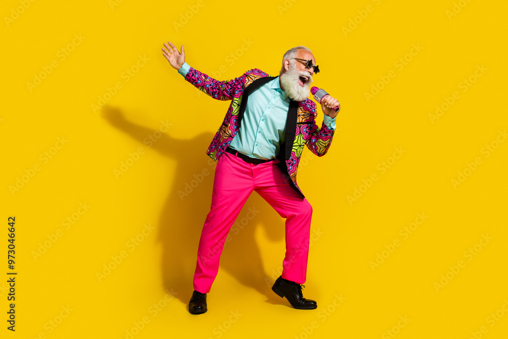 Full size photo of excited aged man sing microphone wear colorful blazer pink pants isolated on yellow background Full size photo of excited aged man sing microphone wear colorful blazer pink pants isolated on yellow background