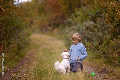 Cute little blond child, boy, training his little pet dog to obey orders, playing with him outdoors