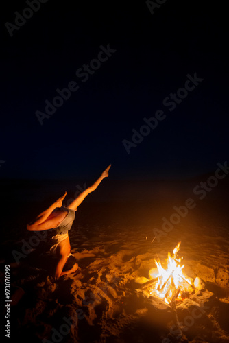 fit girl does yoga on a beach at dusk next to a bonfire