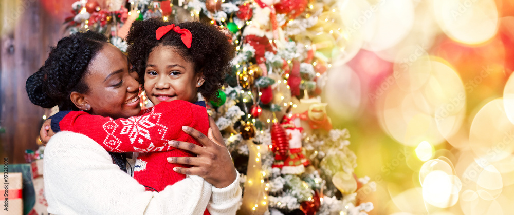 Cute little afro girl cuddling with her mom near Christmas tree, celebrating winter holidays at home. Cute little afro girl cuddling with her mom near Christmas tree, celebrating winter holidays at home.