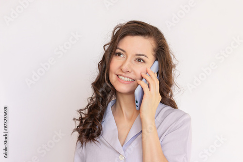 Happy young Caucasian brunette businesswoman with curly hair wearing a purple blouse smiling and talking on the cell phone. She is negotiating successfully