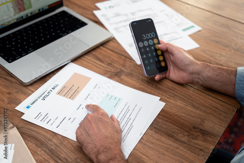 Close-up of a man calculating household utility bills using a smartphone. Financial management and budgeting concept for household expenses and utility bills photo