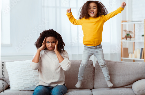 Tableau sur toile Tired Mother Covering Ears Having Headache While Daughter Jumping On Couch At Home