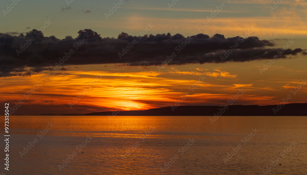Golden sunset over Isle of Arran in the Firth of Clyde sea with band of dark cloud in sky Golden sunset over Isle of Arran in the Firth of Clyde sea with band of dark cloud in sky