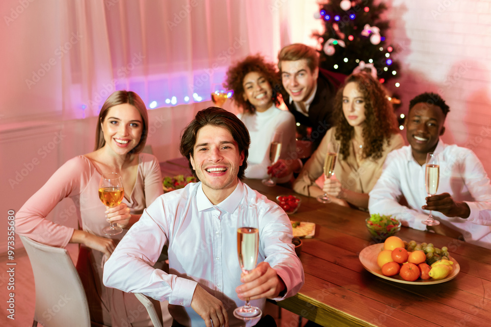 Obraz premium Happy New Year. Millennial Friends Holding Champagne Glasses Toasting Looking At Camera Sitting At Dinner Table At Home.