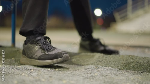 Wallpaper Mural Close-up of a person's feet as they repeatedly tap on the ground, with a blurred, dimly lit background and an iron railing visible in the distance Torontodigital.ca