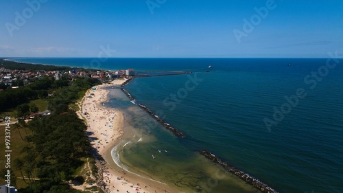 Golden beach, calm Baltic waters, sunbathers, swimmers, and ships from Darłowo port, captured by a drone.