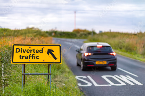 Tableau sur toile Car passing yellow diverted traffic sign at slow bend on country road