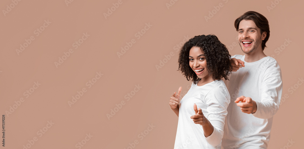 Cheerful guy and girl pointing at camera with fingers, choosing somebody, standing together over yellow studio background Cheerful guy and girl pointing at camera with fingers, choosing somebody, standing together over yellow studio background