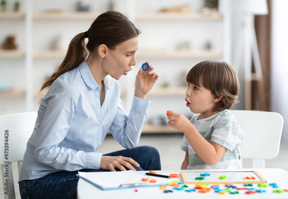 Female speech therapist curing child's problems and impediments. Little boy learning letter O with private English language tutor during lesson at office Female speech therapist curing child's problems and impediments. Little boy learning letter O with private English language tutor during lesson at office