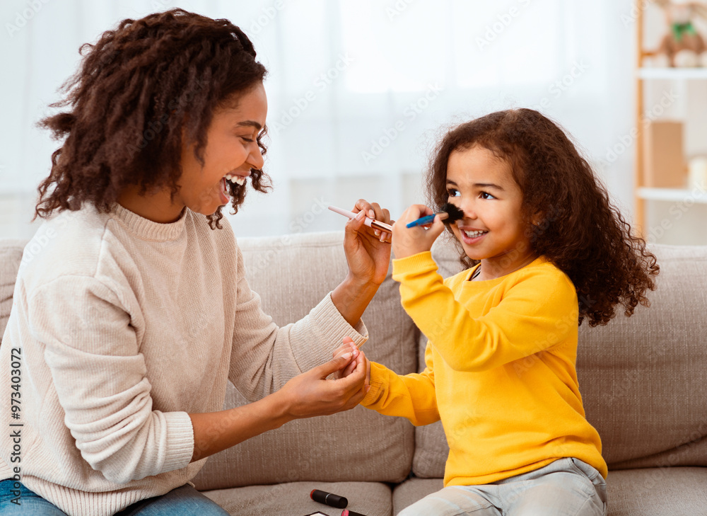 Black Mother And Little Daughter Making Makeup Together Having Fun Sitting On Sofa Indoor. Family Moments Black Mother And Little Daughter Making Makeup Together Having Fun Sitting On Sofa Indoor. Family Moments
