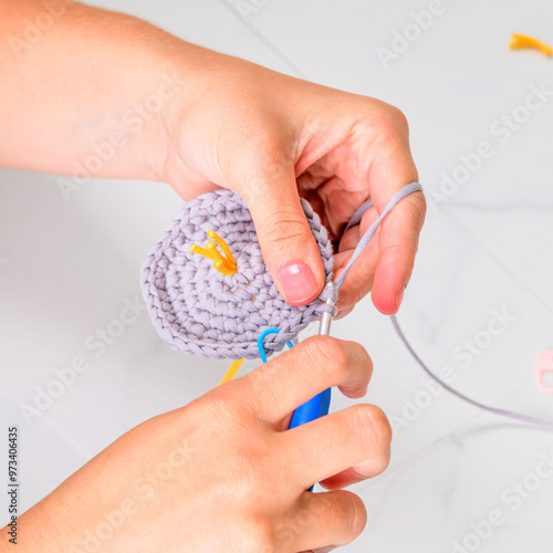 woman crocheting with gray yarn and a blue crochet hook on a white background 