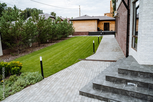 Fotografie This stunningly beautifully landscaped backyard features a charming paved pathwa